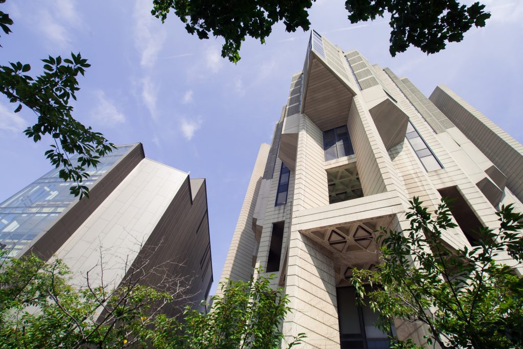 Robarts Library at the University of Toronto is shown surrounded by leafy foliage and backed by blue sky.