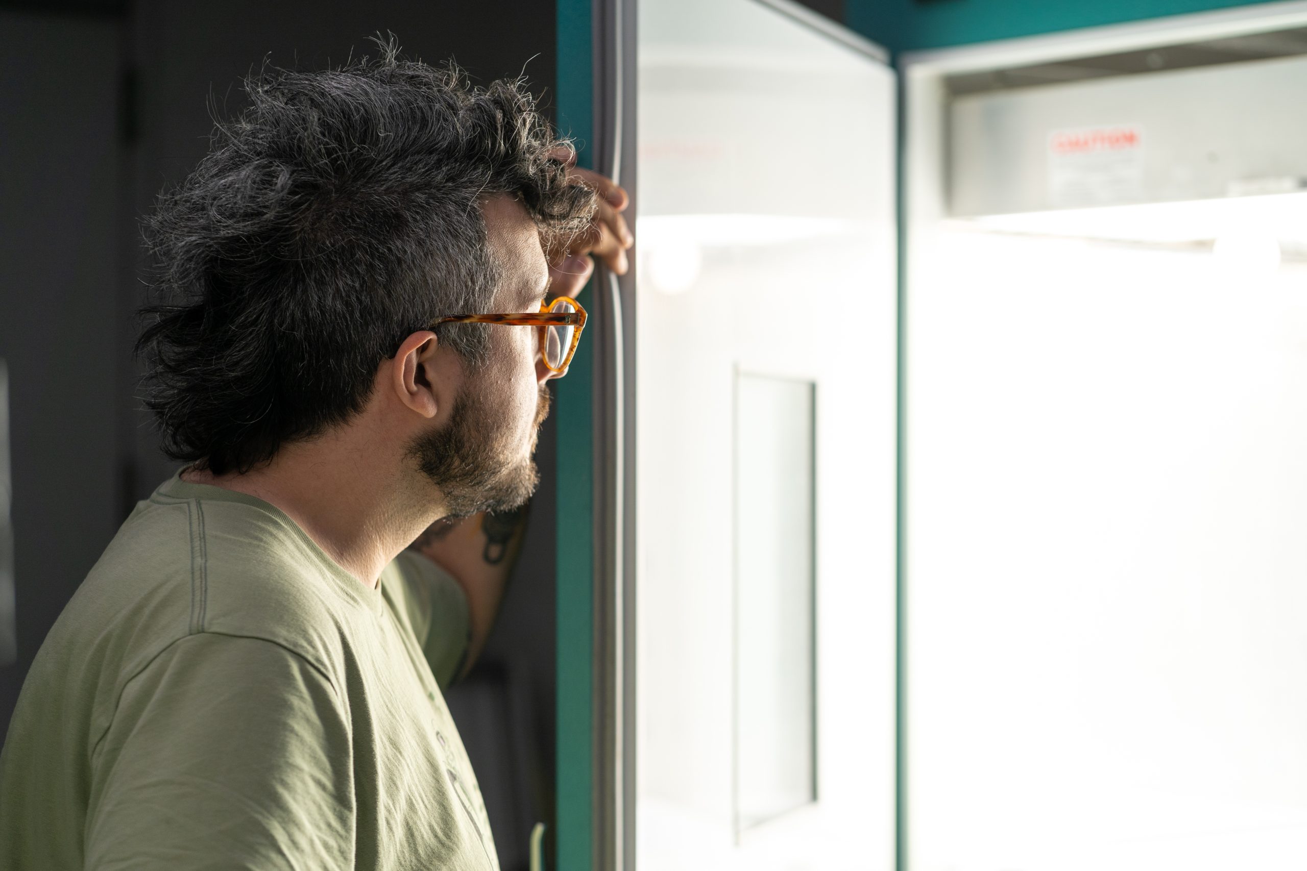 A man wearing glasses looks into a brightly lit chamber with the solid metal door swung open.